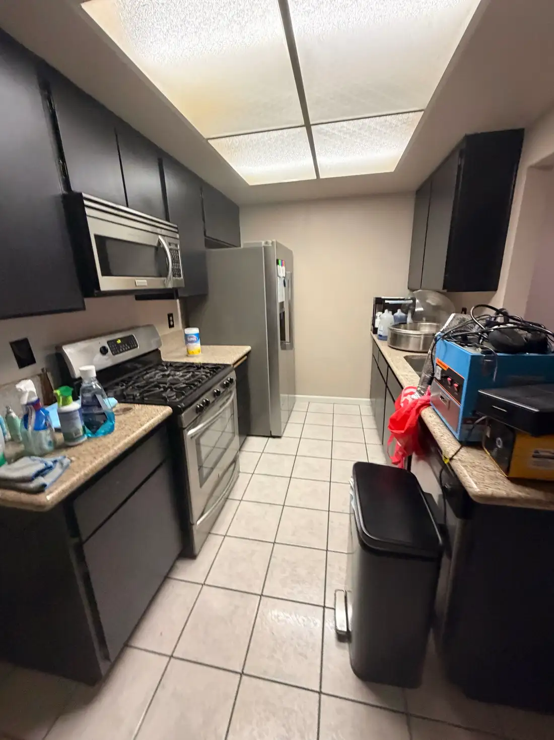 The rental's kitchen before: dark cabinets, tiled floor and a cluttered counter